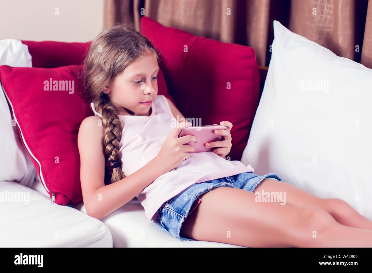 Bambina gioca con un telefono cellulare a casa su un divano Foto Stock