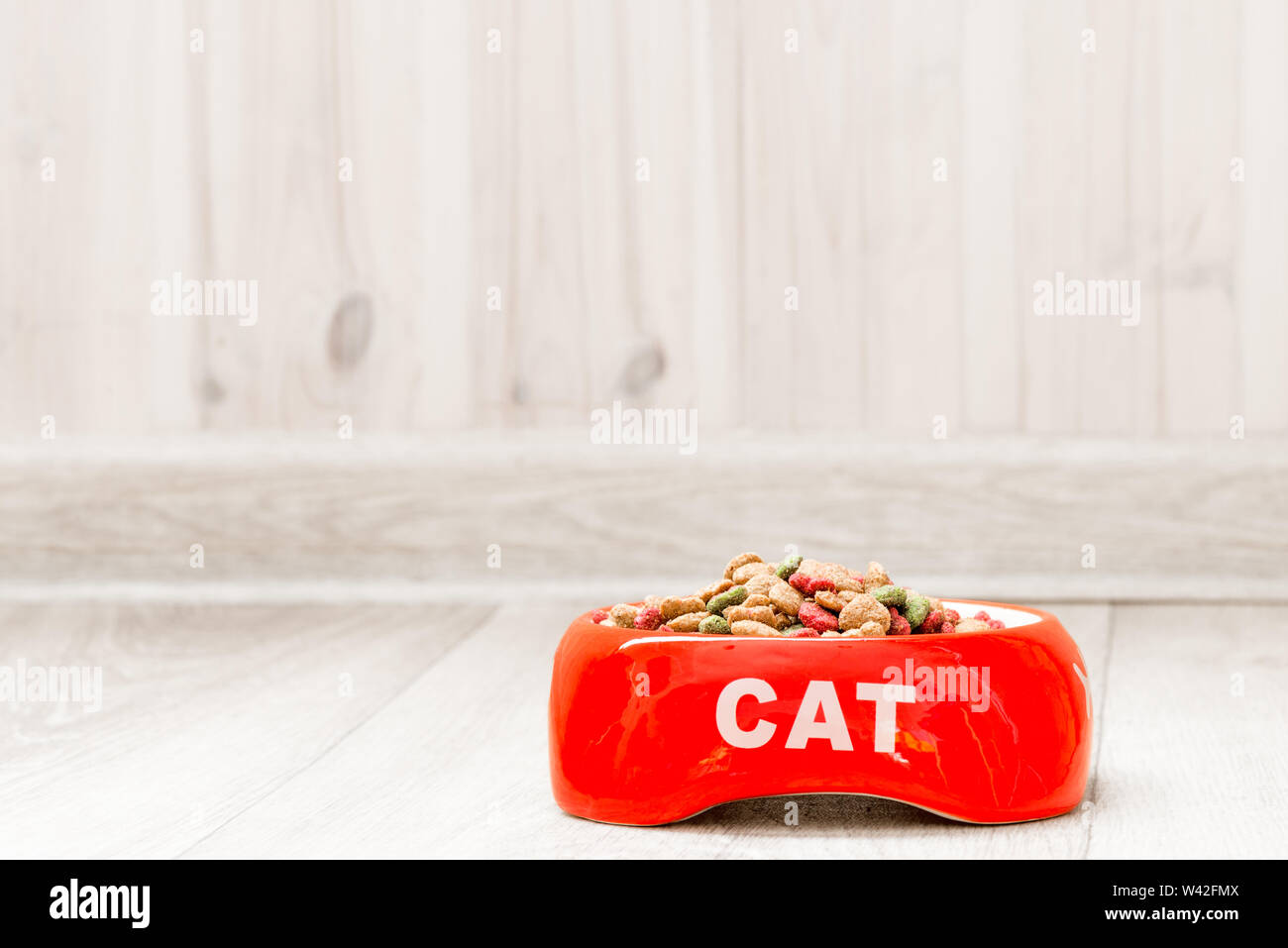 Recipiente rosso per un gatto con cibo secco sul pavimento della casa di close-up Foto Stock