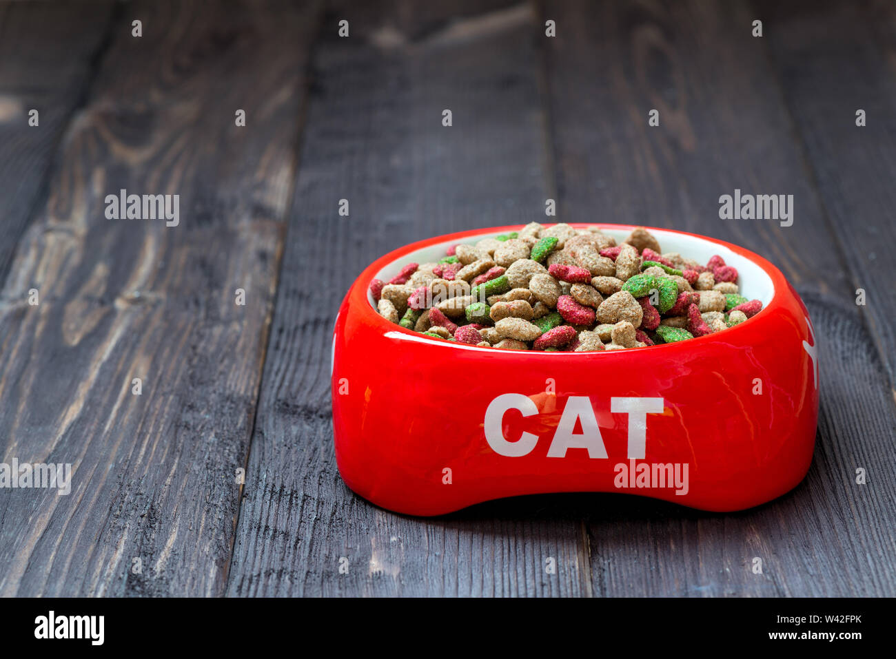 Su un pavimento di legno un recipiente rosso per un gatto con cibo secco Foto Stock