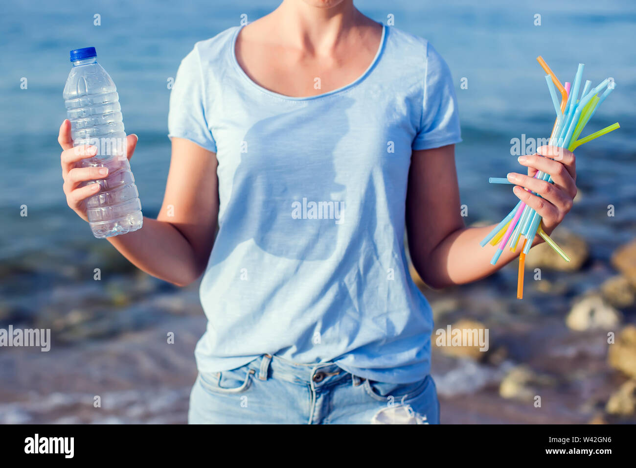 La donna mantiene la bottiglia di plastica e le cannucce in mani sulla spiaggia. Plastica concetto dell'inquinamento. Foto Stock