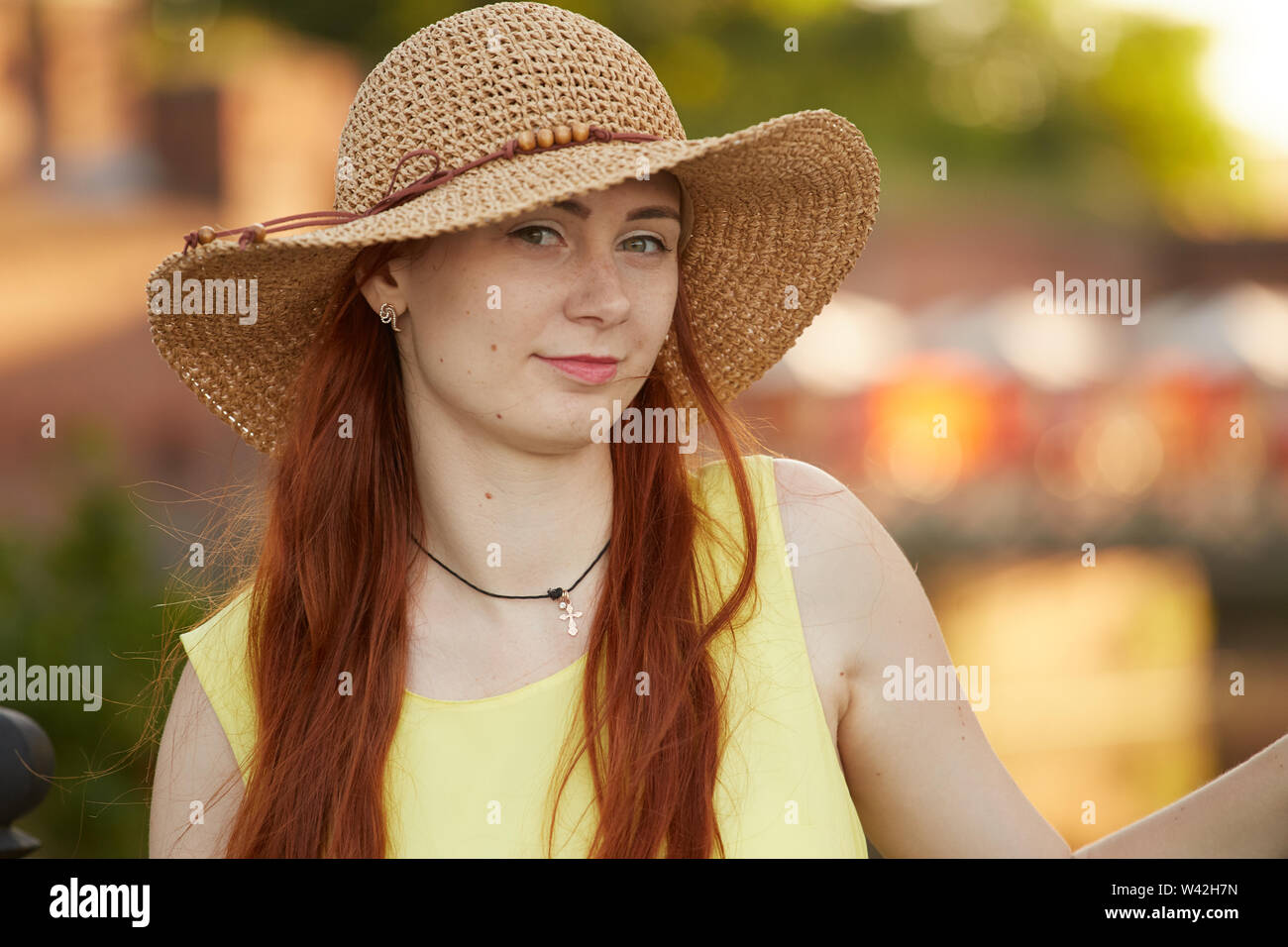 Bella Capelli rossi ragazza nel cappello per il sole guardando la telecamera, sorridente Foto Stock