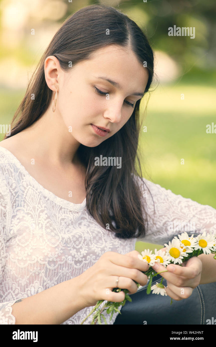 Bella ragazza con lunghi capelli bruna rendendo omaggio floreale con camomiles Foto Stock