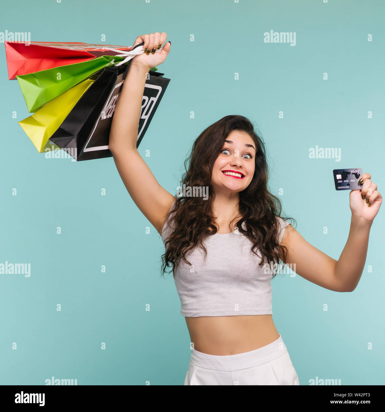 Funny donna con pacchetti multicolori e la carta di credito su uno sfondo giallo, shopping - Immagine Foto Stock