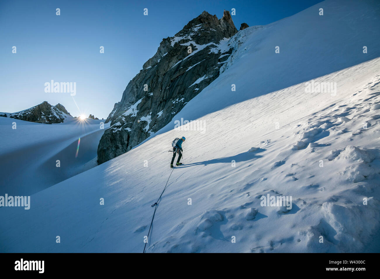Un alpinista affronta un ripido pendio di neve come il sole creste l'orizzonte Foto Stock