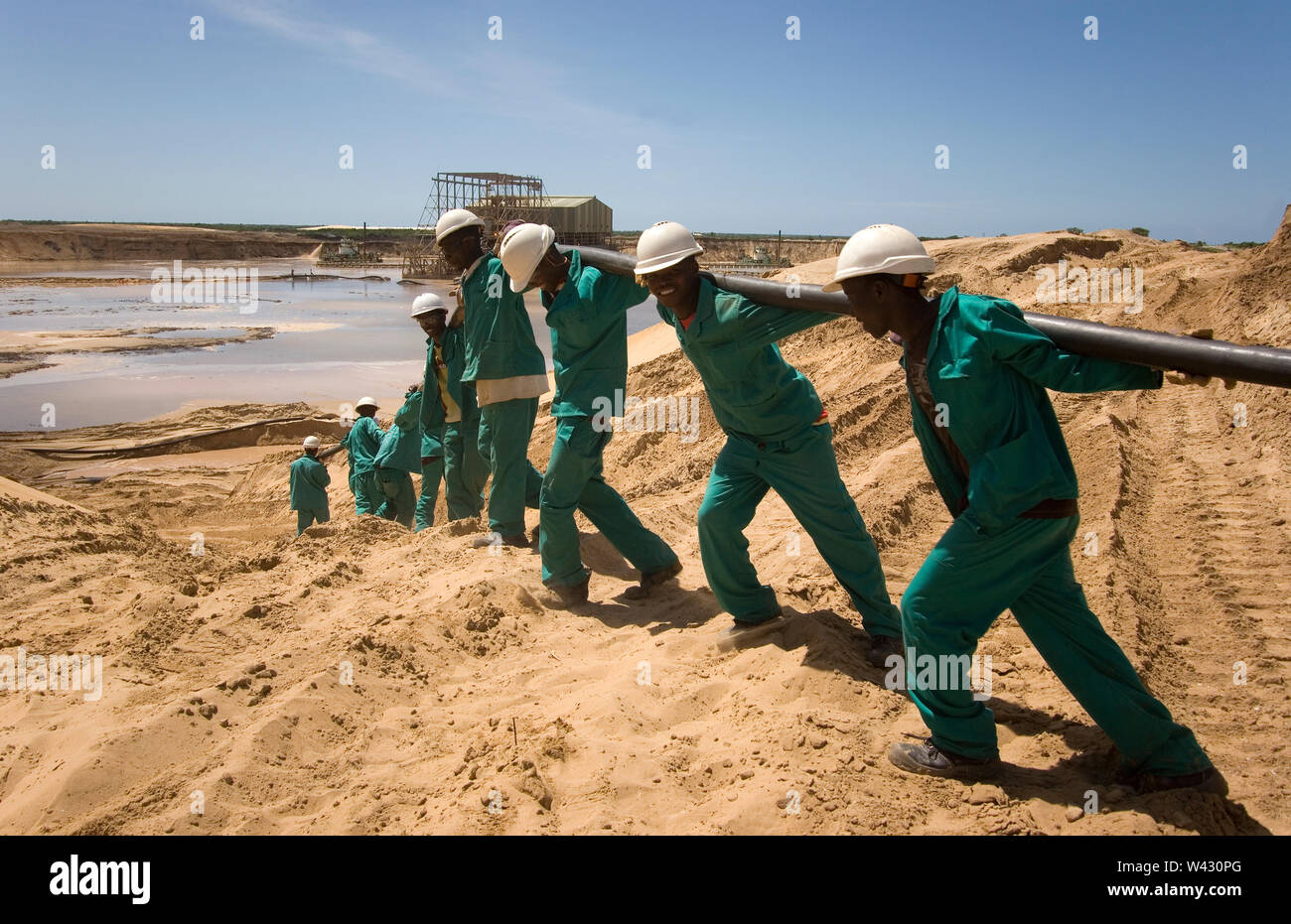 Estrazione, gestione e trasporto di sabbie minerali di titanio. Team di manutenzione che posa nuovi cavi di alimentazione sul lato del laghetto di estrazione per impianti umidi dietro. Foto Stock