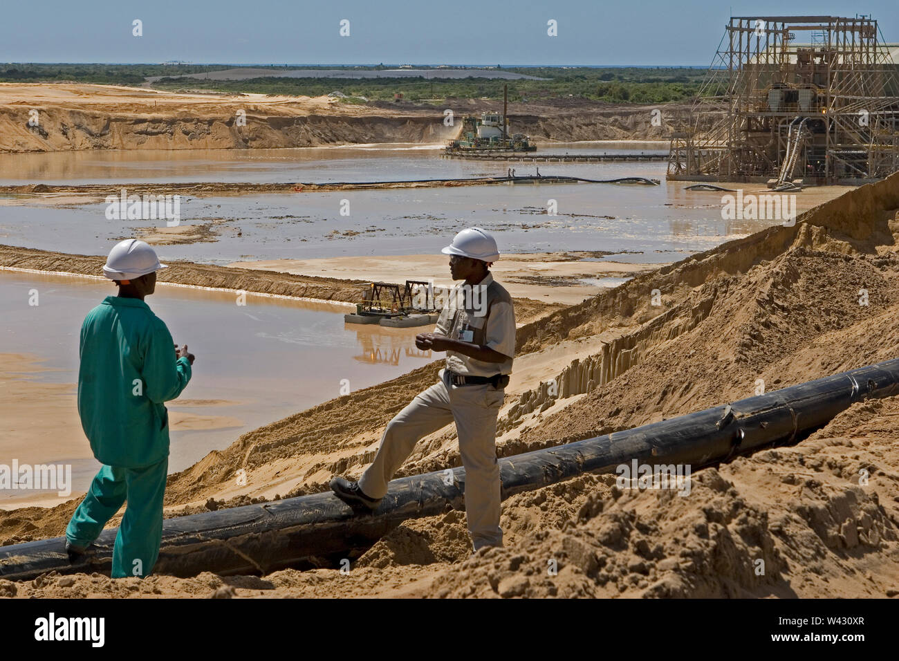 Gestione e trasporto di sabbie minerali di titanio nel sito minerario. Estrazione mineraria utilizzando draghe che pompano sabbia da acqua stagno più supervisore formazione nuovo lavoratore. Foto Stock