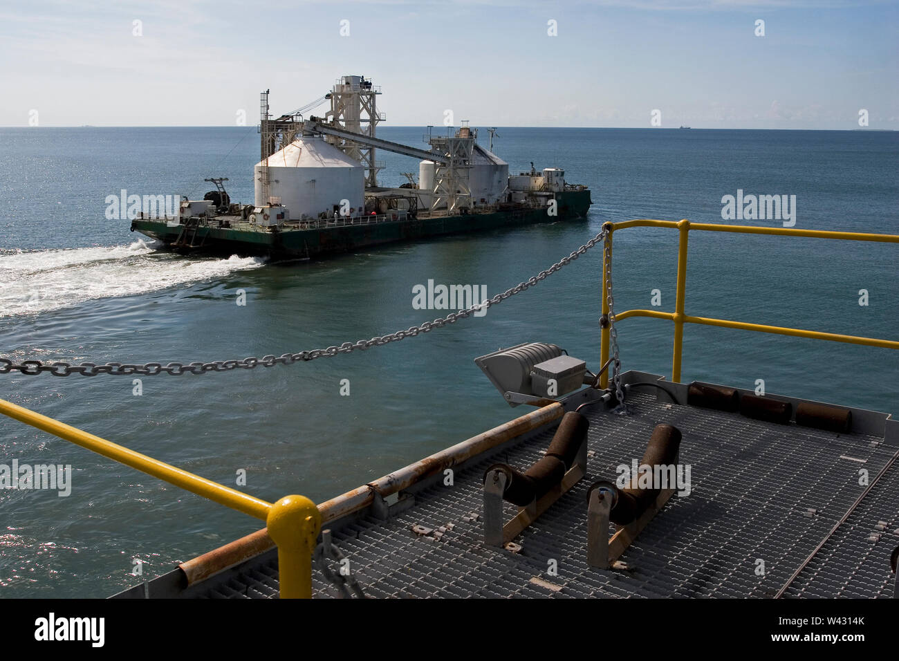 Estrazione, gestione e trasporto di sabbie minerali di titanio. Chiatta che lascia il porto per OGV in mare - mostra infrastrutture del molo e molo galleggiante sotto. Foto Stock