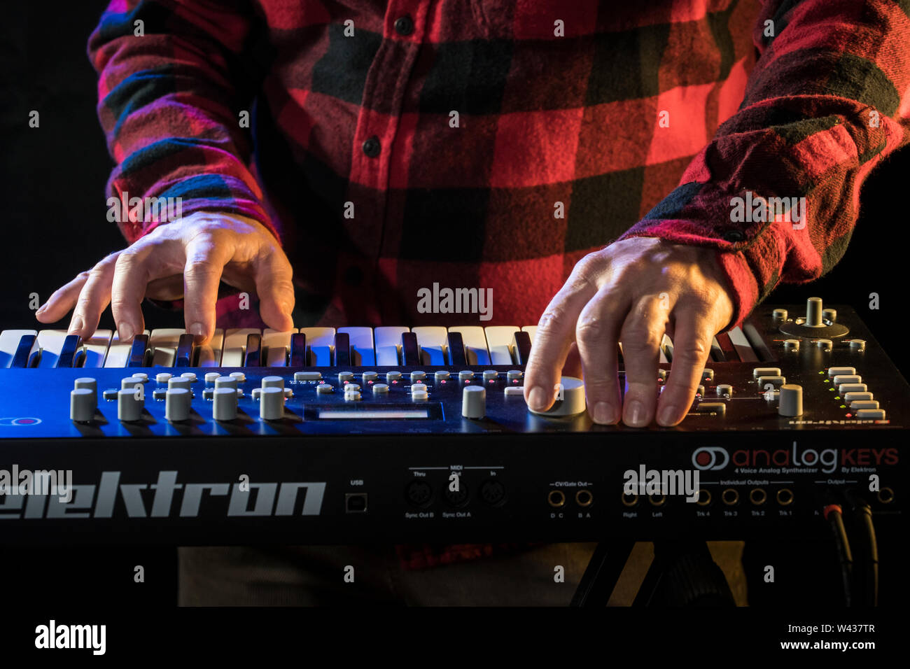 Un musicista che gioca un Elektron analogico sintetizzatore di chiavi con blu e arancione illuminazione scenica. Foto Stock