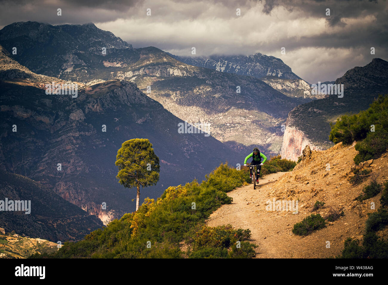 Un uomo corse in mountain bike su un isolato sterrato nelle Montagne Atlas. Alte montagne e rainclouds in background. Foto Stock