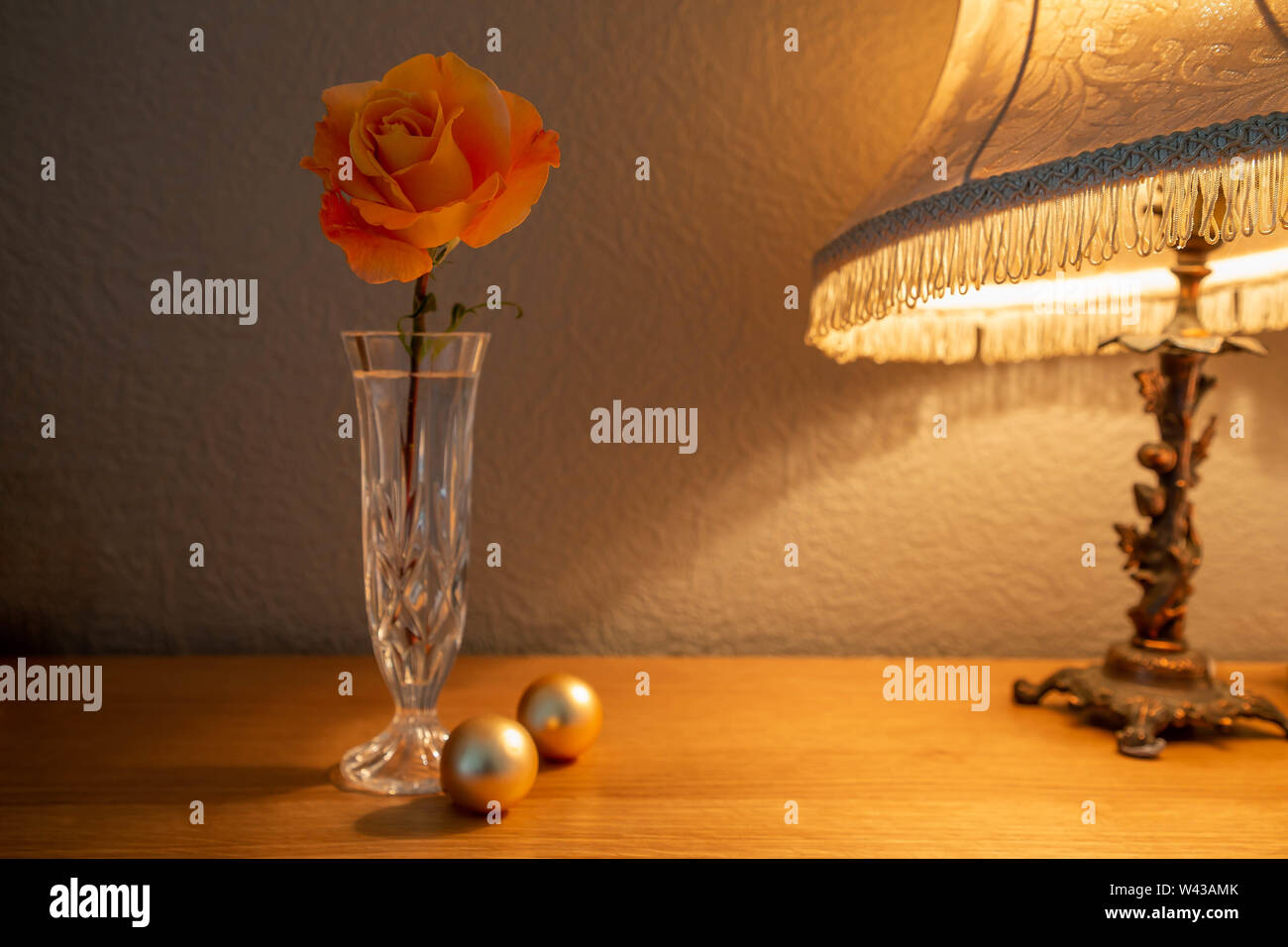 Un grande Whisky Mac Hybrid Tea Rose fiori recisi in un taglio vaso di vetro illuminato da una lampada da tavolo Foto Stock
