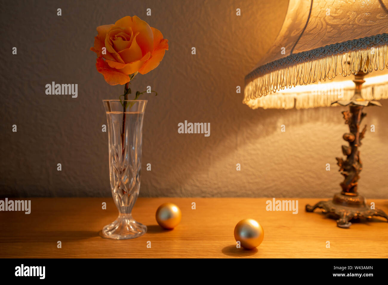 Un grande Whisky Mac Hybrid Tea Rose fiori recisi in un taglio vaso di vetro illuminato da una lampada da tavolo Foto Stock