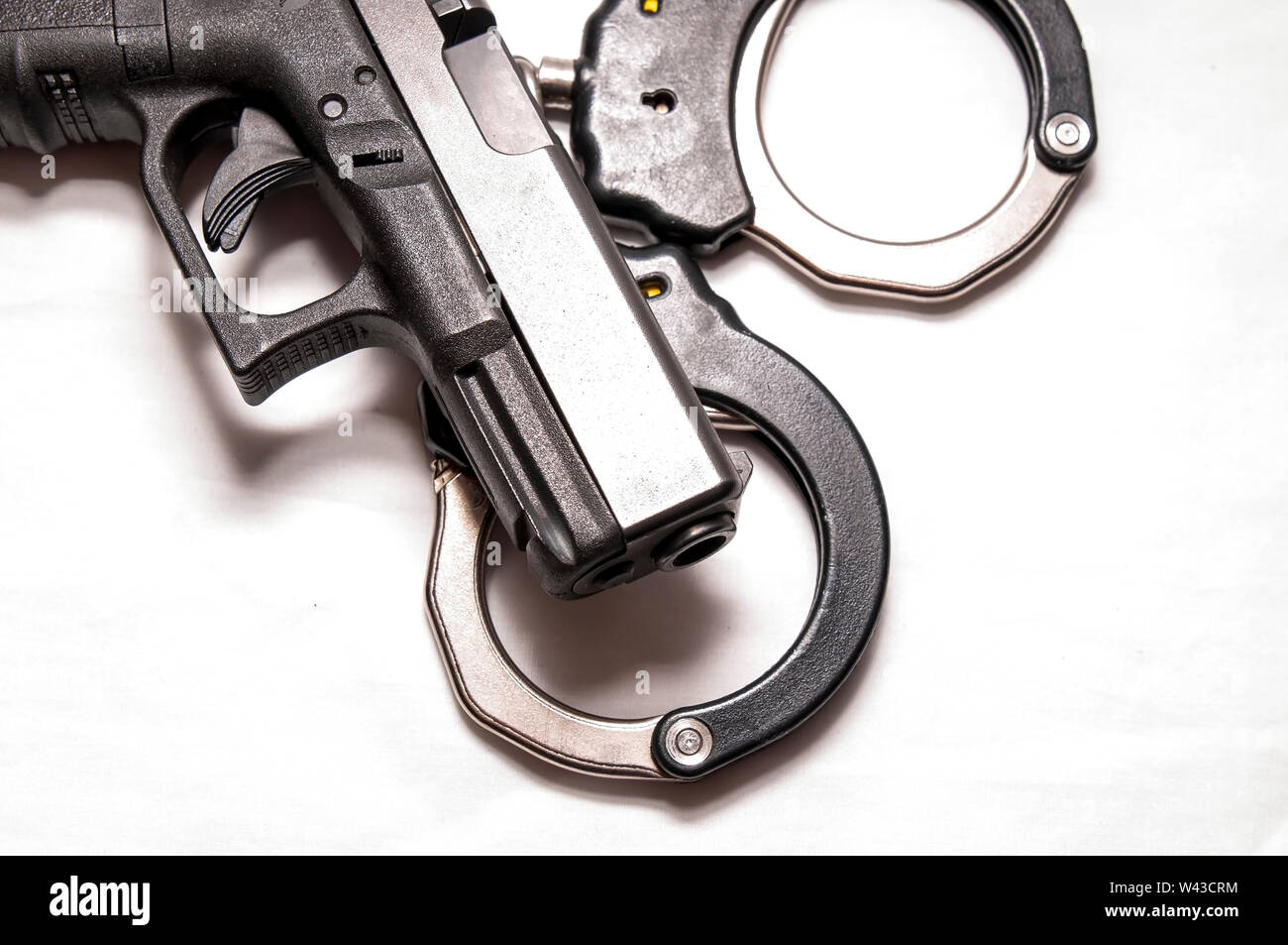 Un nero 9mm pistola sulla sommità di una serie di colori nero e argento manette su sfondo bianco Foto Stock