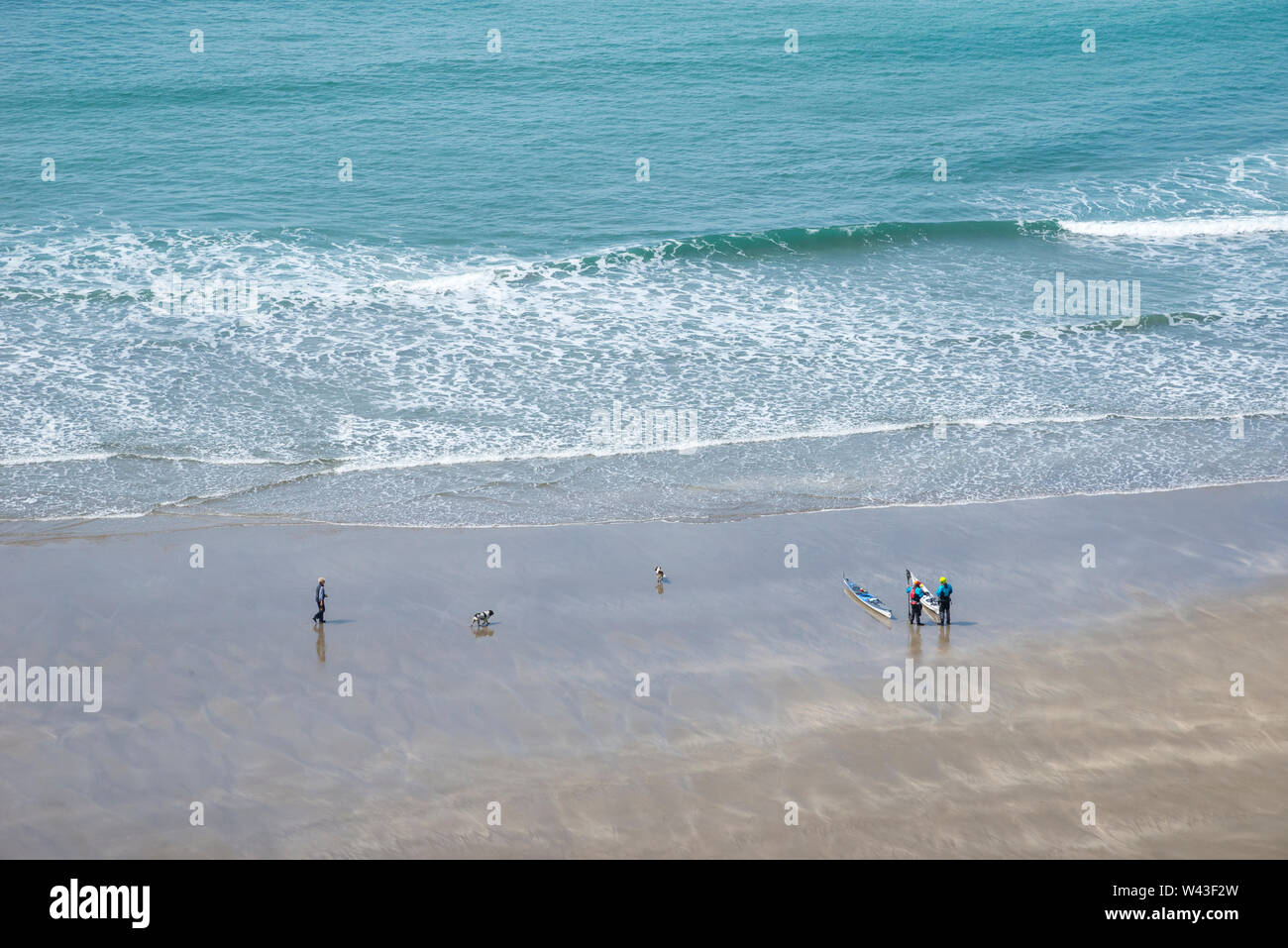 Donna dog walker e due persone con Canoe sulla spiaggia di Traeth Llyfn, Pembrokeshire, Galles. Foto Stock