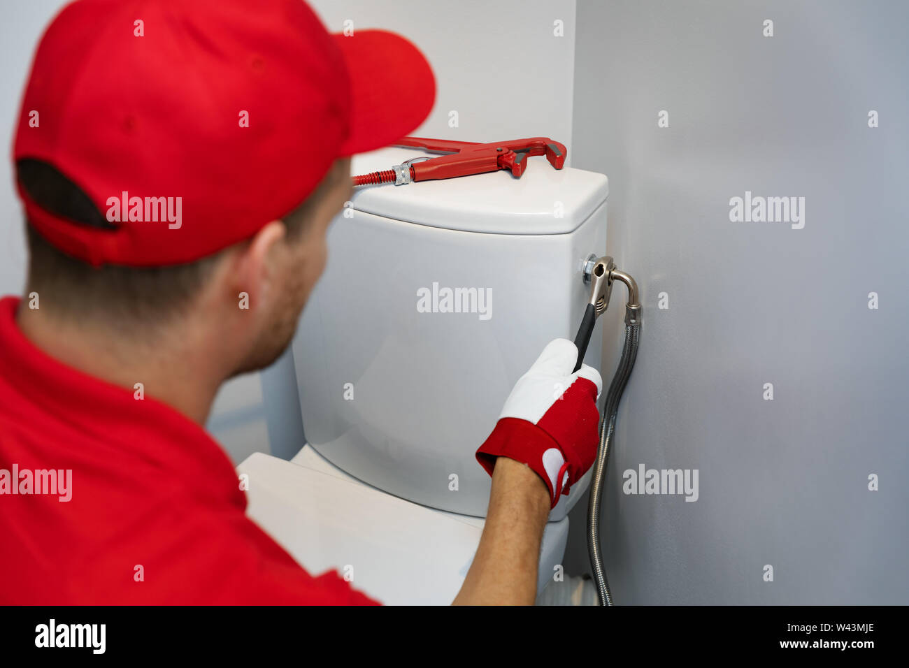 Plumber lavorando in wc installazione flessibile della tubazione dell'acqua al serbatoio wc Foto Stock