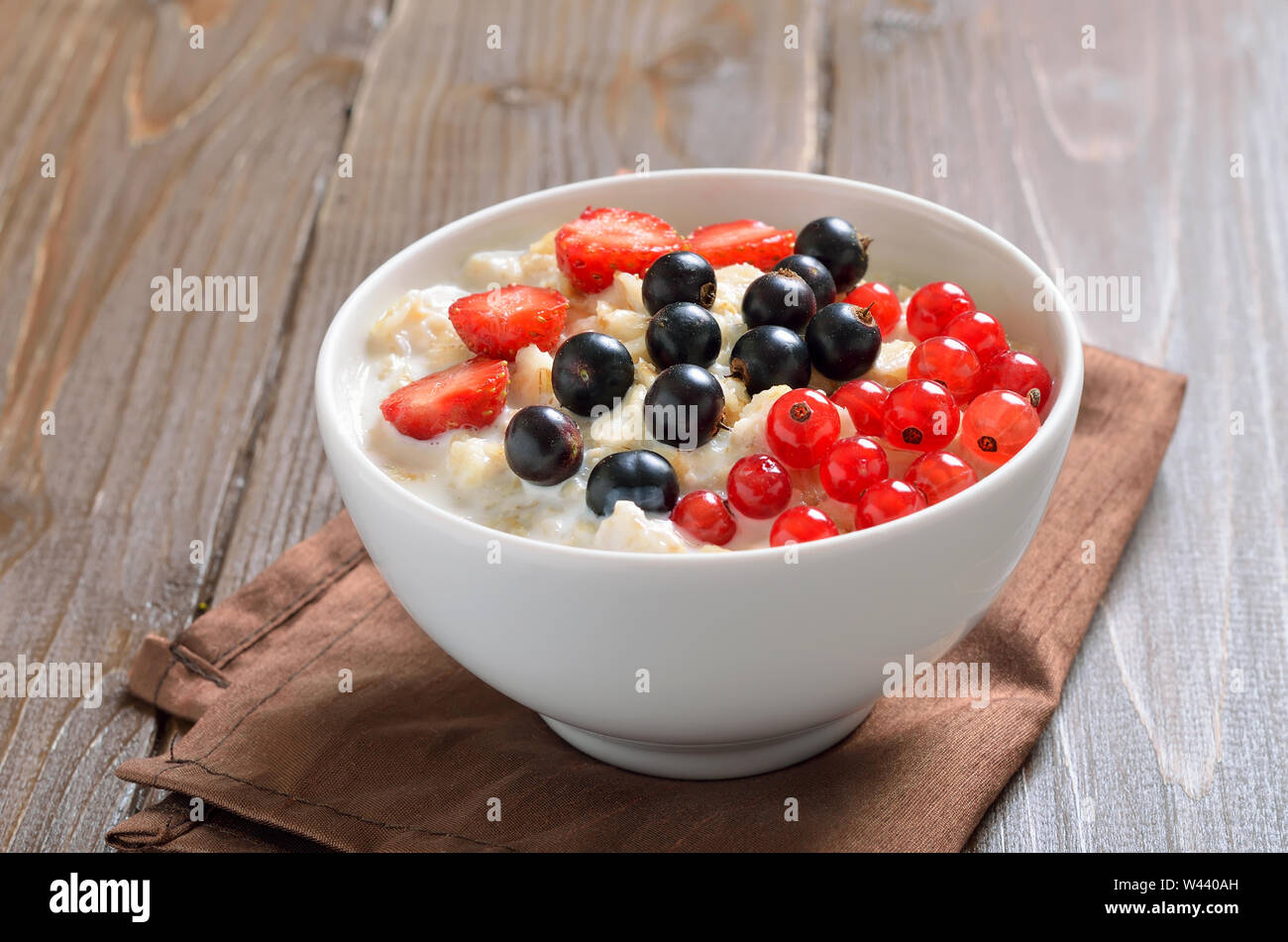 Farina di avena porridge con bacche nella ciotola sul tavolo di legno, vista ravvicinata Foto Stock