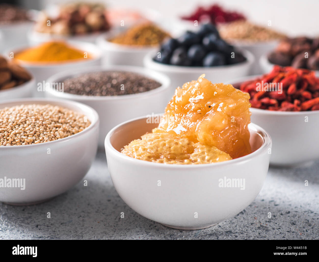 Hive o miele di favo di miele in piccola ciotola bianco e altri superfoods sullo sfondo. Messa a fuoco selettiva. Superfoods diversi ingredienti. Concetto e illustrazione per la super e detox food Foto Stock