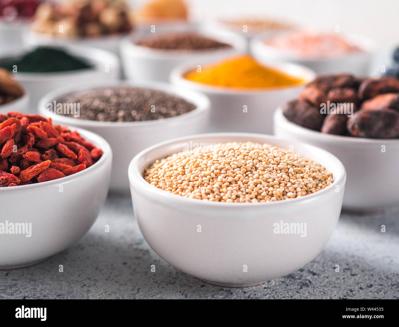 La quinoa in granella piccola ciotola bianco e altri superfoods sullo sfondo. Messa a fuoco selettiva. Superfoods diversi ingredienti. Concetto e illustrazione per la super e detox food Foto Stock