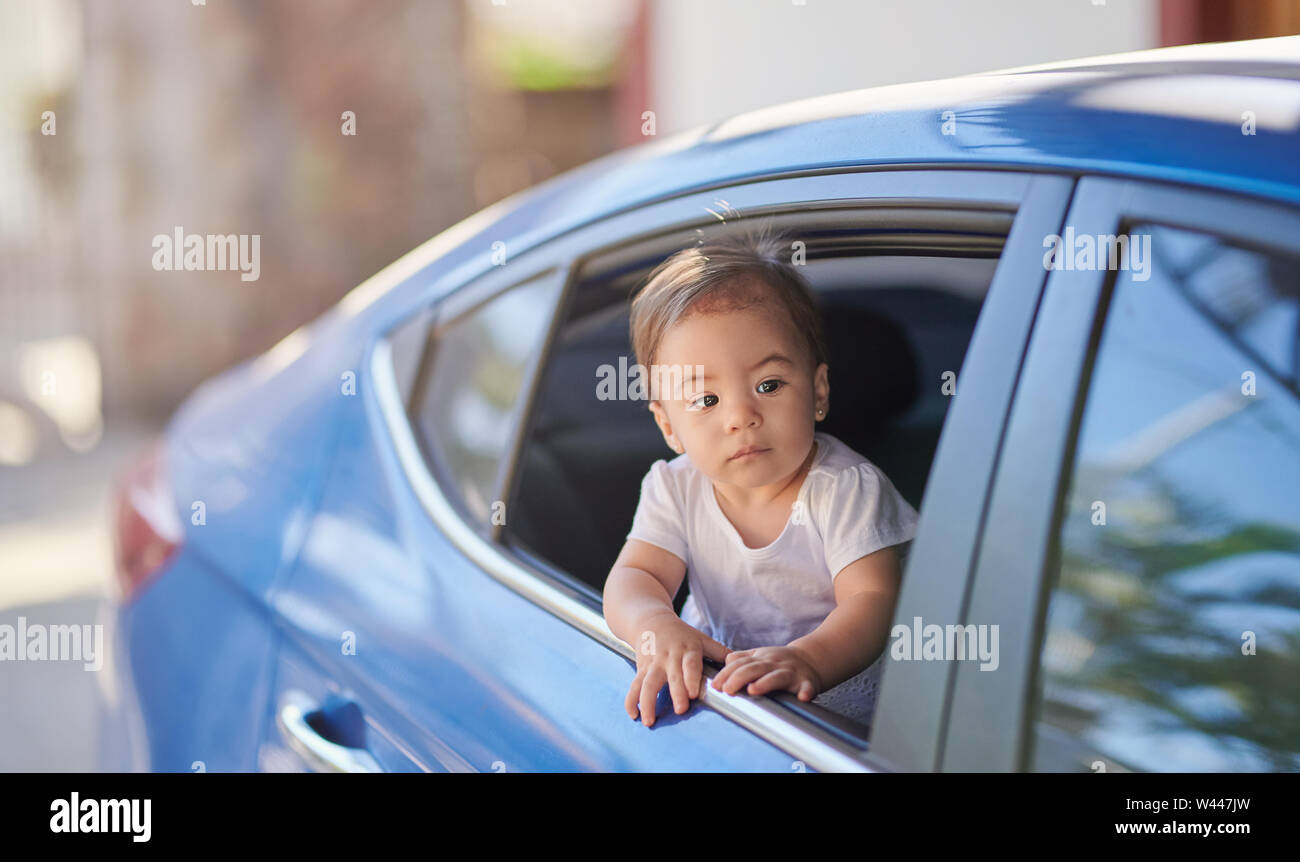 Piccolo bambino in auto nella finestra posteriore guardando avanti su sfondo sfocato Foto Stock