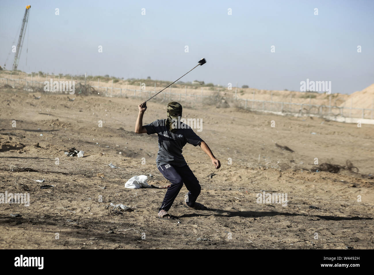 Un dimostrante palestinese utilizza un slingshot per scagliare pietre contro le forze israeliane durante scontri pur dimostrando chiedendo la fine al blocco israeliano della Striscia di Gaza e rivendicano il diritto di tornare alle loro case durante la recinzione di confine tra Israele e la striscia di Gaza nel sud della striscia di Gaza. Foto Stock