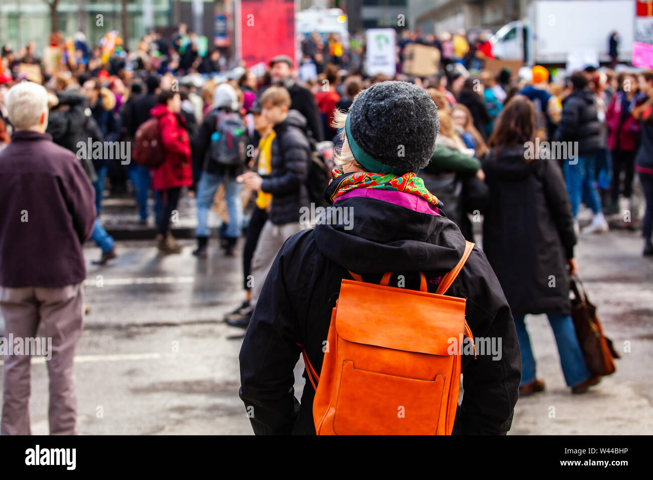 Una donna è visto da dietro, indossando uno zaino arancione e wooly hat, come lei guarda eco-friendly attivisti tappa una dimostrazione nella città. Foto Stock