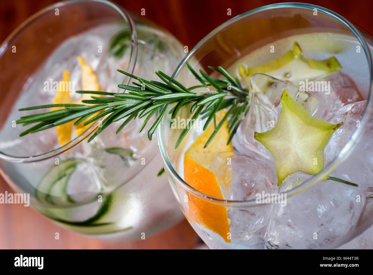 Angolo basso close up di ghiaccio freddo moderne imbarcazioni gourmet cocktail di gin tonic soda guarnita da fetta di limone e rosmarino rametto irrorato da Juniper essere Foto Stock