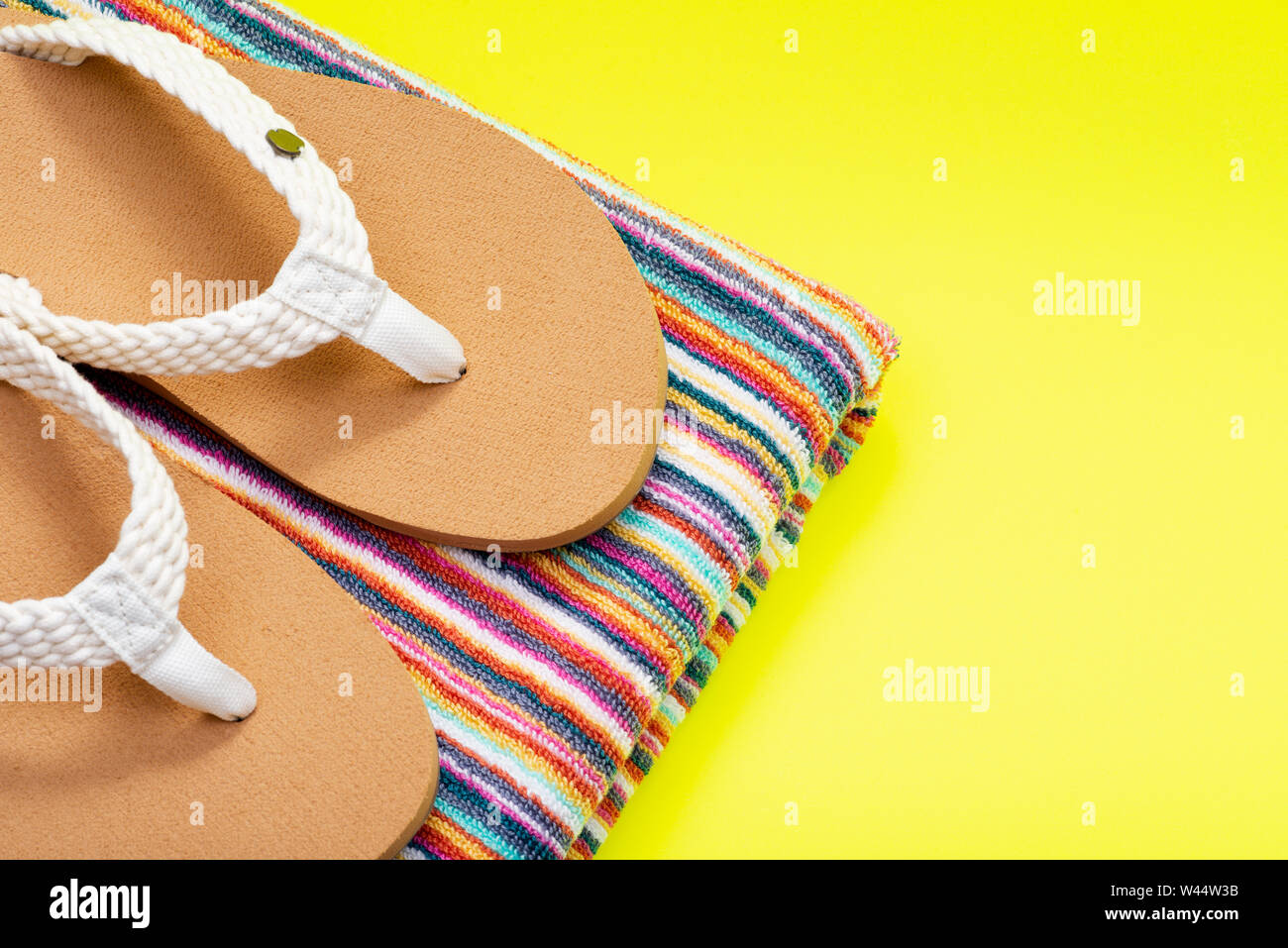 Donna intrecciato causale colore naturale giorno spiaggia Flip Flop e piegato a strisce colorate gli asciugamani da spiaggia luminoso su sfondo giallo. Foto Stock