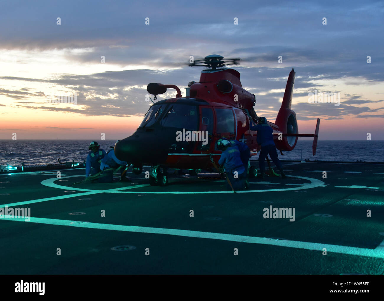 Un tie-down equipaggio a bordo U.S. Guardacoste Bertholf WMSL (750) fissare la nave è avviato MH-65 Delfino elicottero durante la notte le operazioni di sbarco Maggio 25, 2019. La nave è nel mezzo di un pacifico occidentale la distribuzione in sostegno dell'U.S. Marina 7 della flotta. Stati Uniti Coast Guard foto di Chief Petty Officer John Masson. Foto Stock
