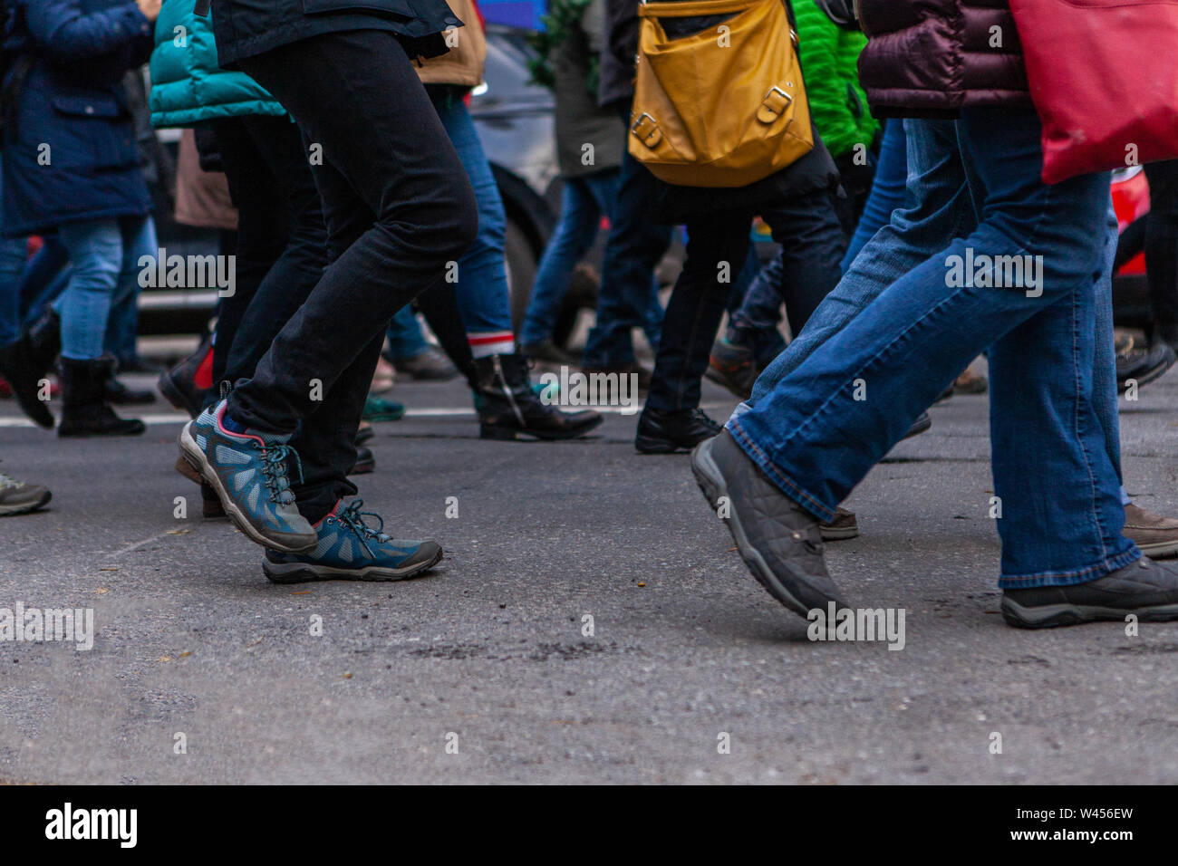 Una vista laterale sulla metà inferiore di un grande gruppo di persone a piedi nella stessa direzione durante una manifestazione contro il cambiamento climatico su una strada. Foto Stock