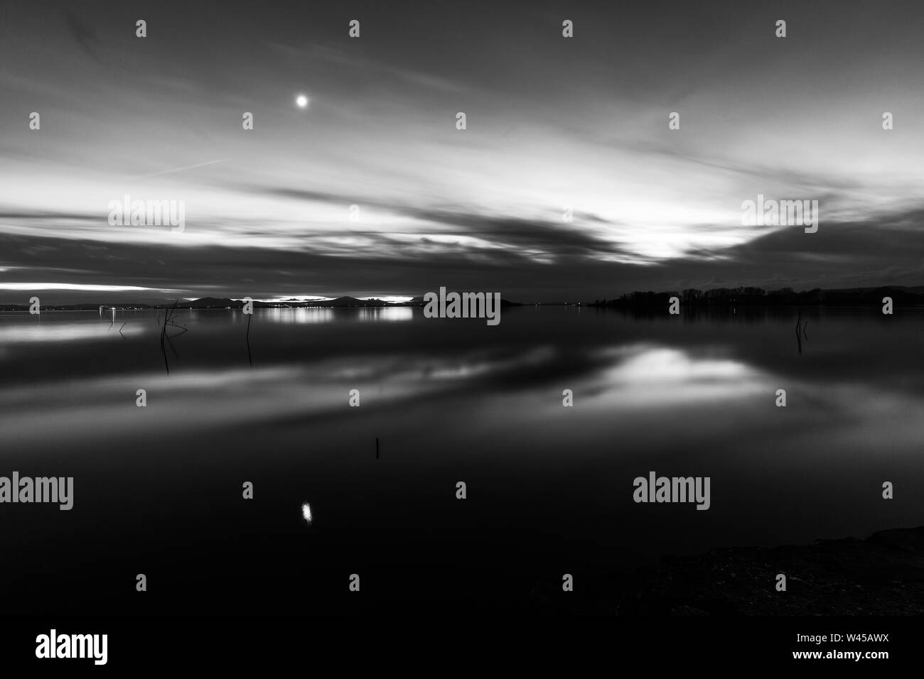 Luna al di sopra di un lago con la sua riflessione sul lago Trasimeno superficie al crepuscolo Foto Stock