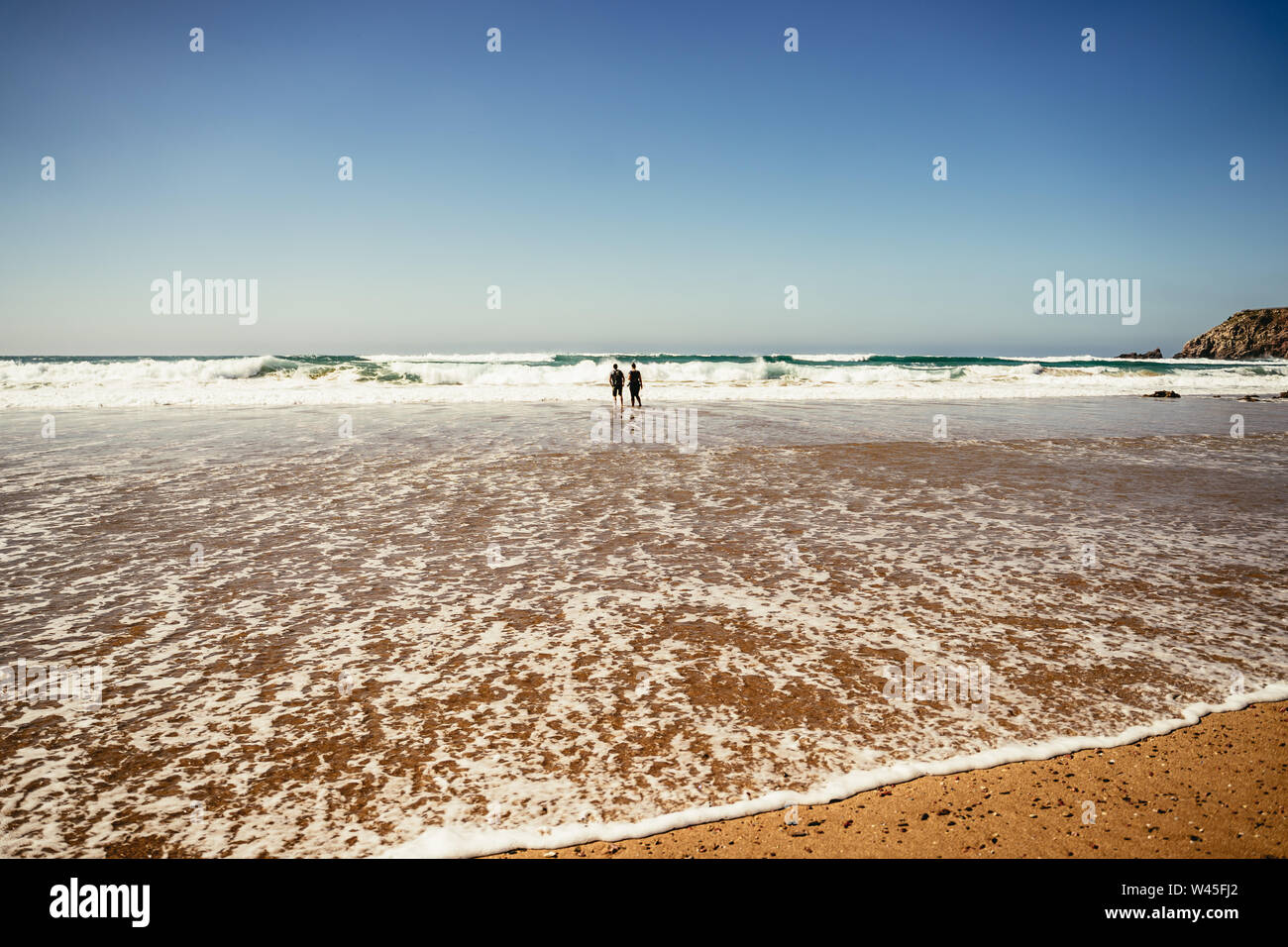Due persone che camminano in surf poco profondo lungo una spiaggia Foto Stock