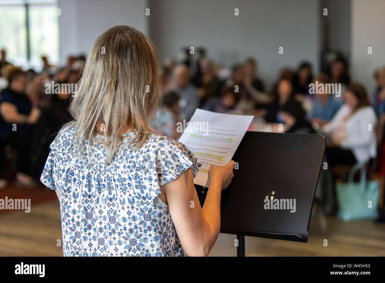 Un oltre la spalla di un altoparlante collocando un discorso su un podio durante una grande riunione di ufficio. Sfocata i colleghi sono visti sullo sfondo. Foto Stock