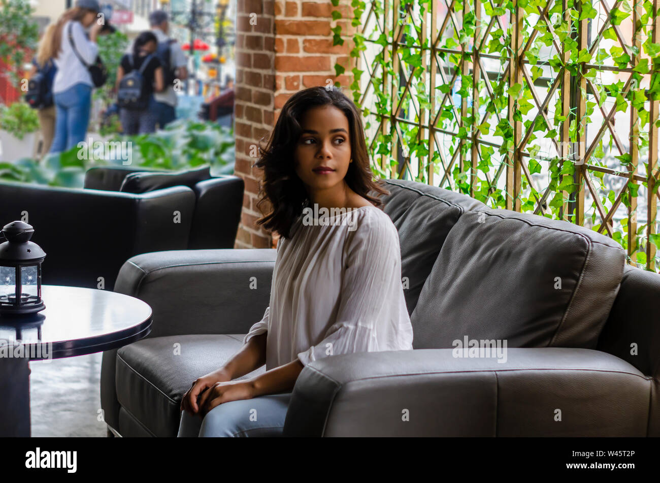 Ragazza giovane dai 19 ai 25 anni seduto sul divano nero nel ristorante guardando fuori dalla finestra di attesa per il suo partner Foto Stock