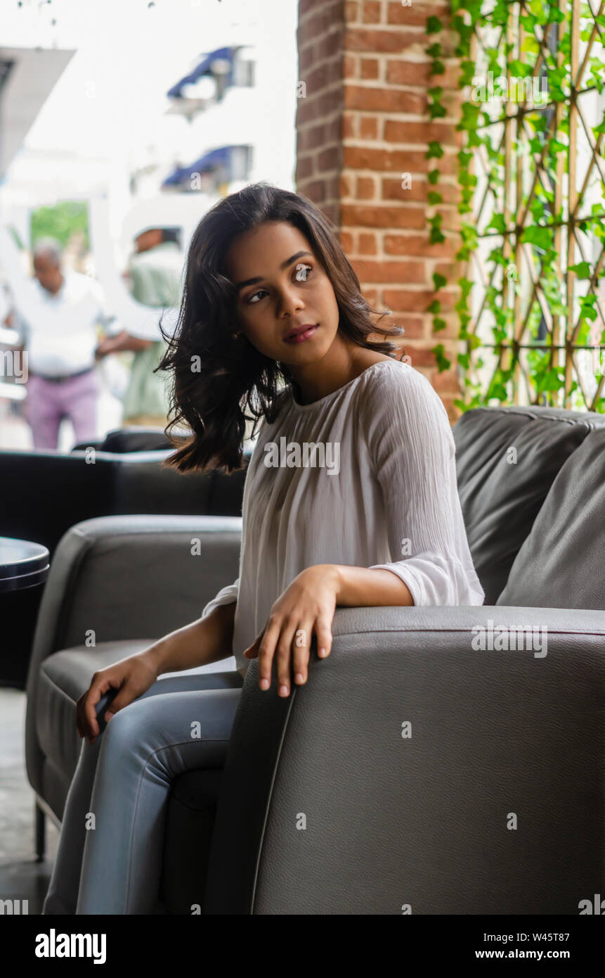 Ragazza giovane dai 19 ai 25 anni seduto sul divano nero nel ristorante guardando fuori dalla finestra di attesa per il suo partner Foto Stock