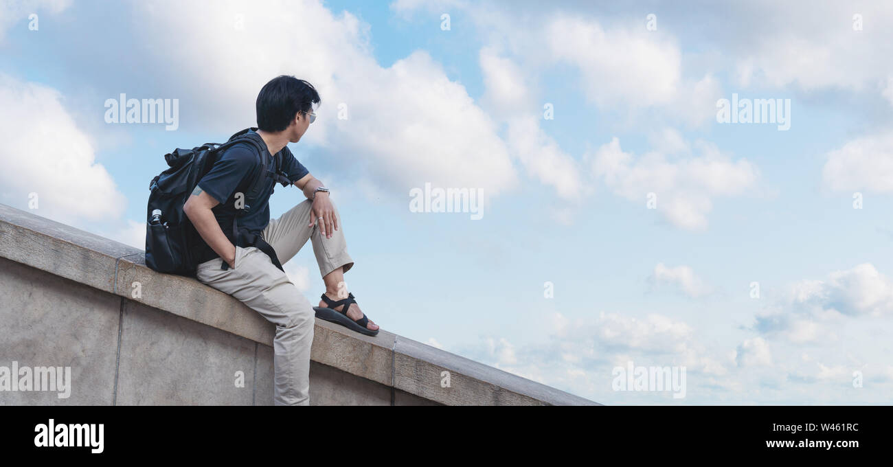 Un uomo con zaino guardando il cielo blu e nuvole bianche in estate Foto Stock