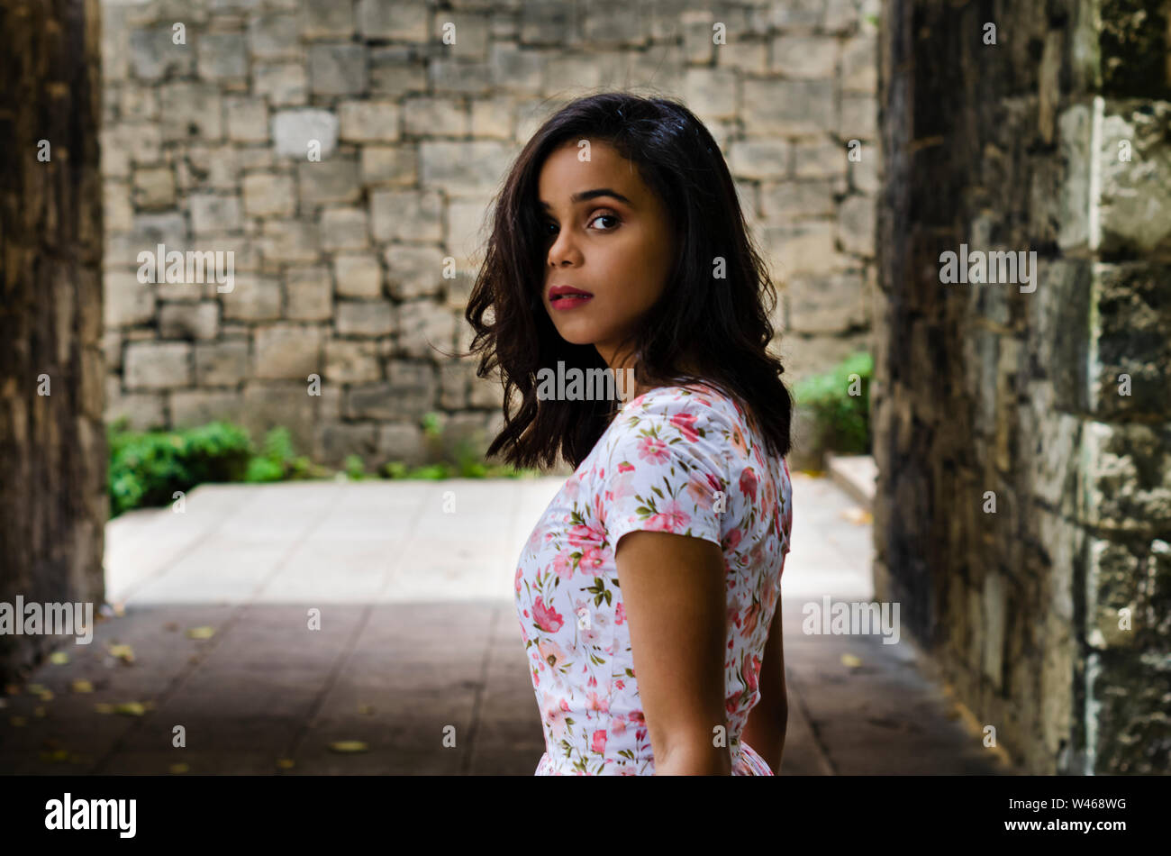 Outdoor Ritratto di giovane bella ragazza 19 a 25 anni. Bruna. passando per la fotocamera con una profonda occhiata. Indossa un fresco abito floreale. Lo stile di vita della città Fe Foto Stock