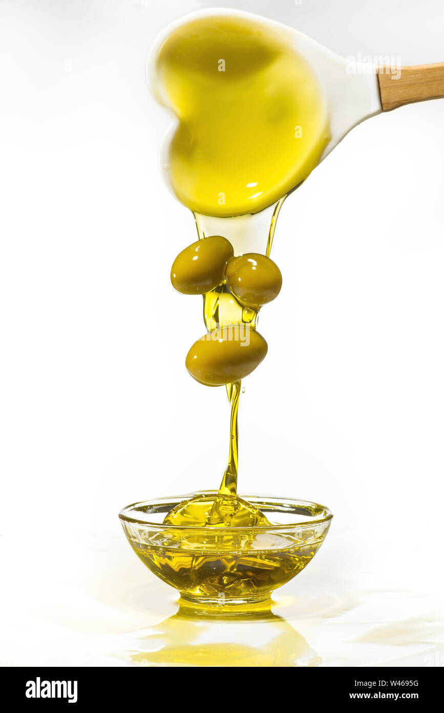 Da un cucchiaio, con la forma di un cuore, alcune olive verdi rientrano in una ciotola piena di olio di oliva con splash. Sfondo bianco Foto Stock