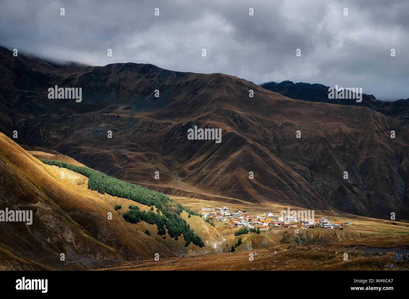 Raggio di sole ne illumina villaggio sulla collina di maggiore montagne del Caucaso a Kazbegi in autunno, Georgia. Foto Stock