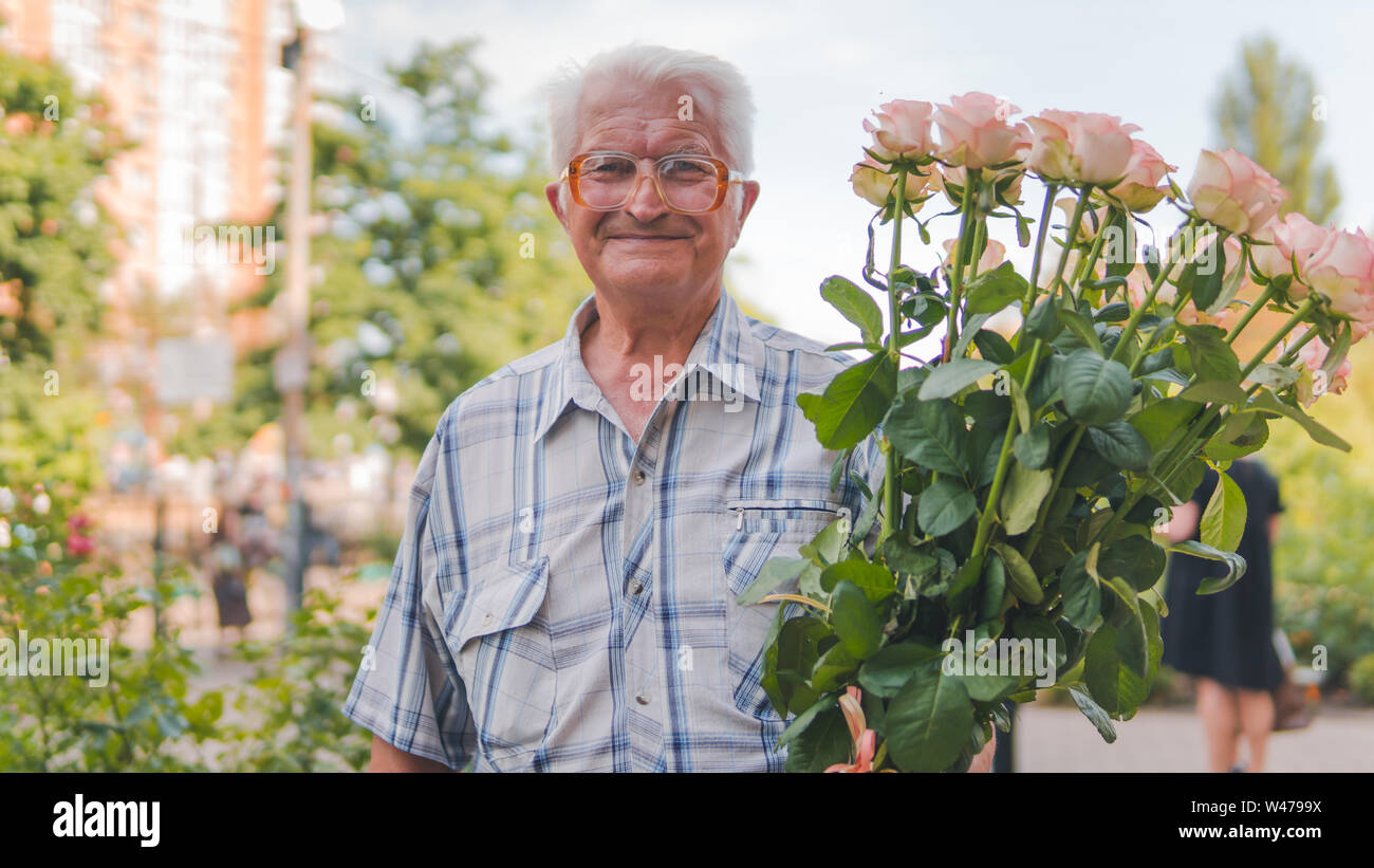 Ritratto di un uomo anziano in piedi sulla strada con un bouquet di rose. Close-up verticale sul vecchio uomo, all'aperto Foto Stock