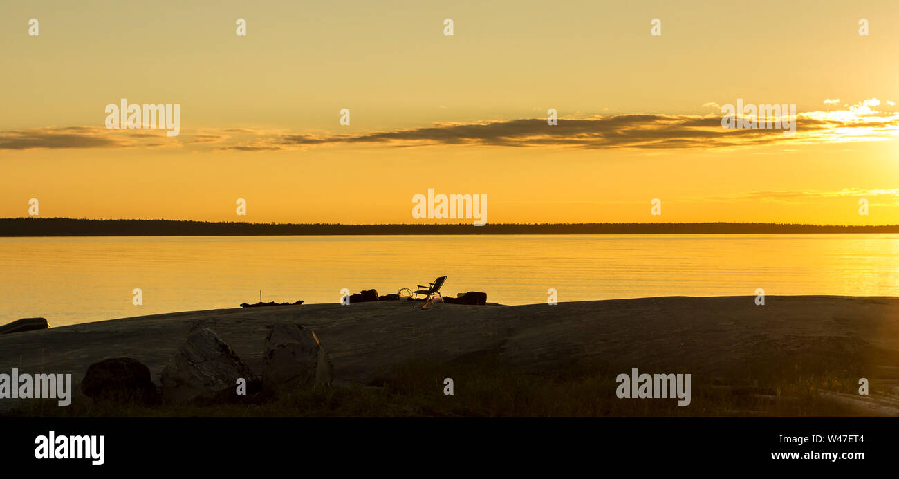 Silhouette di chaise lounge sulla spiaggia. Silent mare calmo al tramonto la Carelia, la Russia. Arancione sfondo naturale Foto Stock
