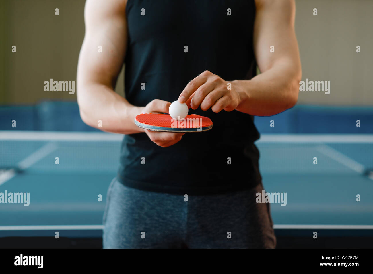 Persona di sesso maschile detiene il racket e ping pong palla su di esso, allenamento indoor. Uomo in sportswear sulla formazione nella tabella-tennis club Foto Stock