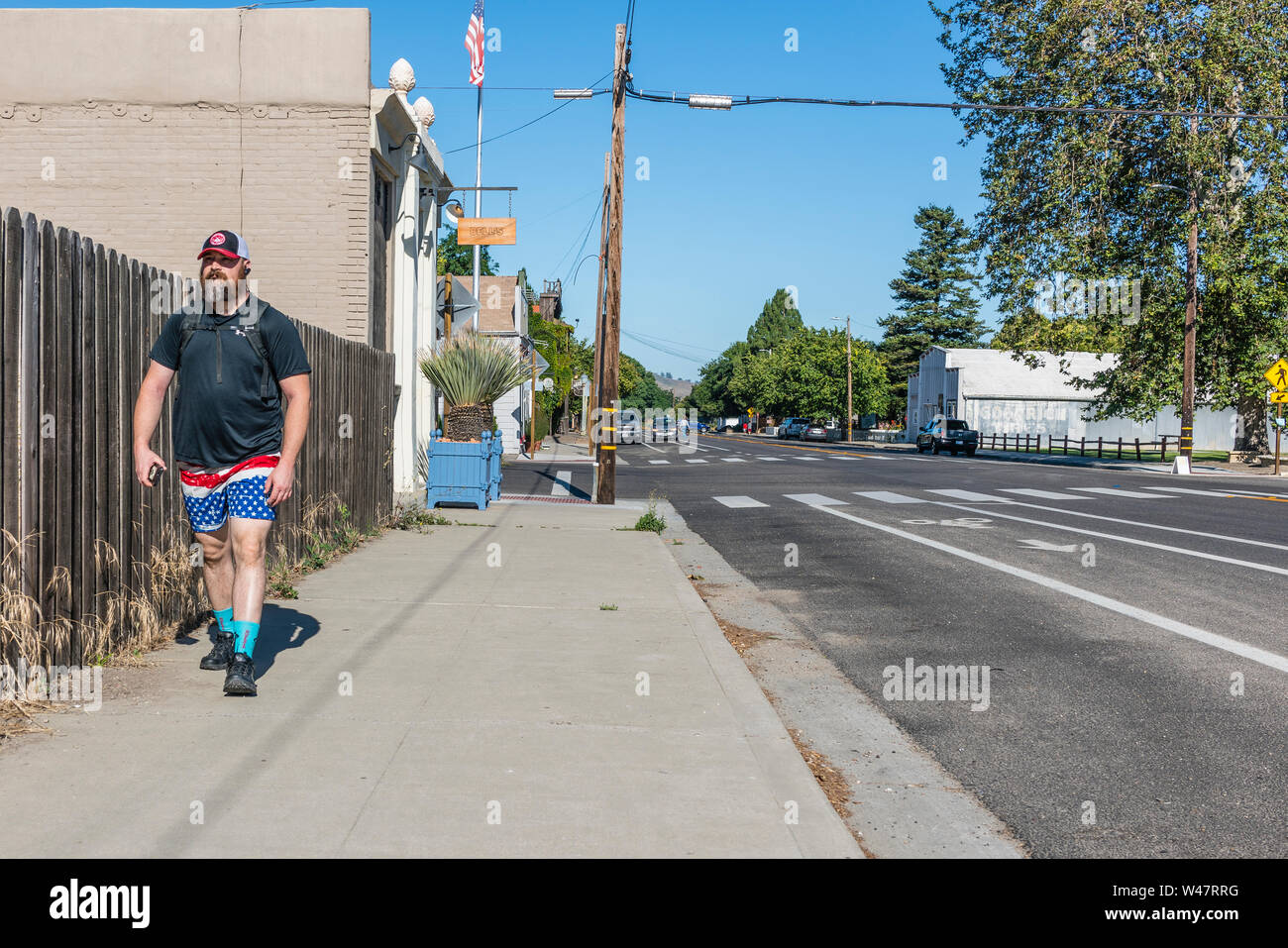 Una mezza età maschio caucasico passeggiate lungo un marciapiede indossando rosso, bianco e blu shorts in un pattern simile alla bandiera americana. Foto Stock