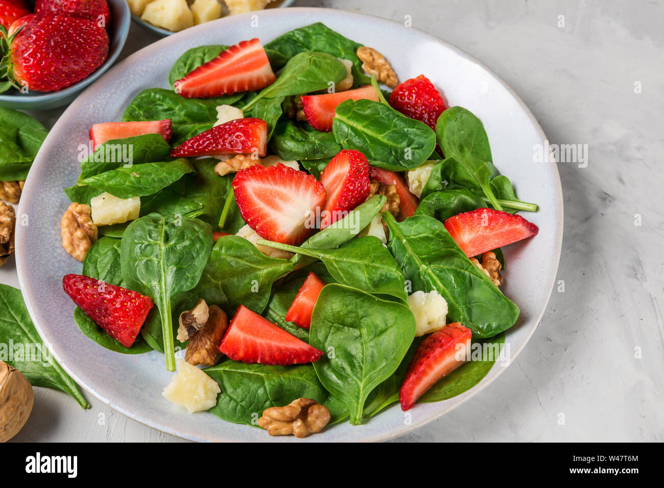 Con insalata di fragole, foglie di spinaci, formaggio parmigiano e noci su calcestruzzo sfondo. una sana dieta alimentare. close up Foto Stock