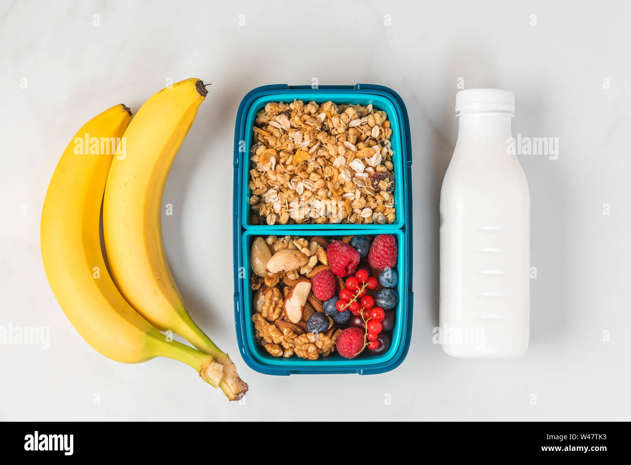 Una sana scatola di pranzo con muesli, dadi, bacche, banana e yogurt per fare una sana prima colazione su sfondo bianco. vista superiore Foto Stock