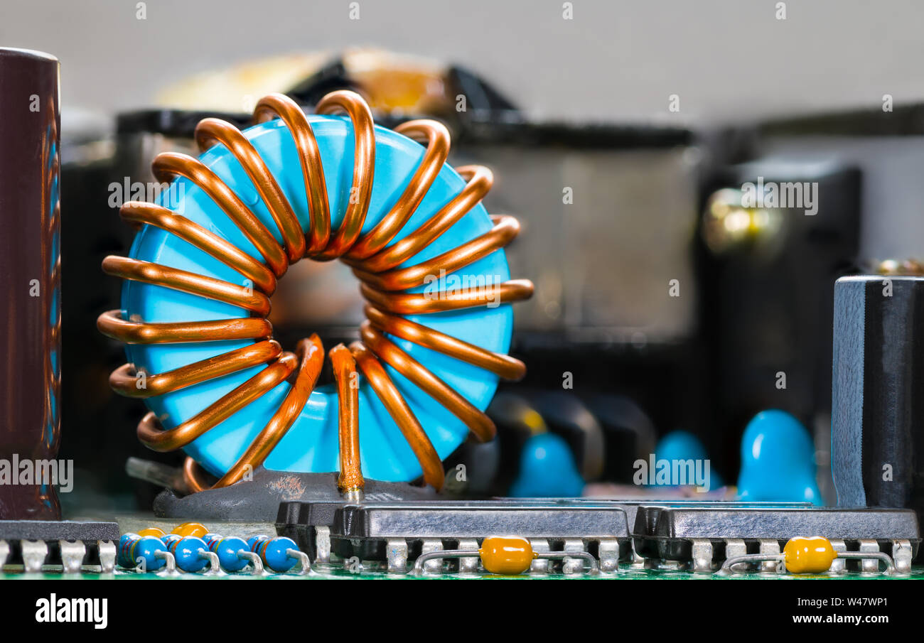 Blu del nucleo della bobina di avvolgimento in filo di rame su circuiti integrati. Induttore toroidale particolare e microchip. Componenti elettronici su circuito stampato. Elettrotecnica. Foto Stock
