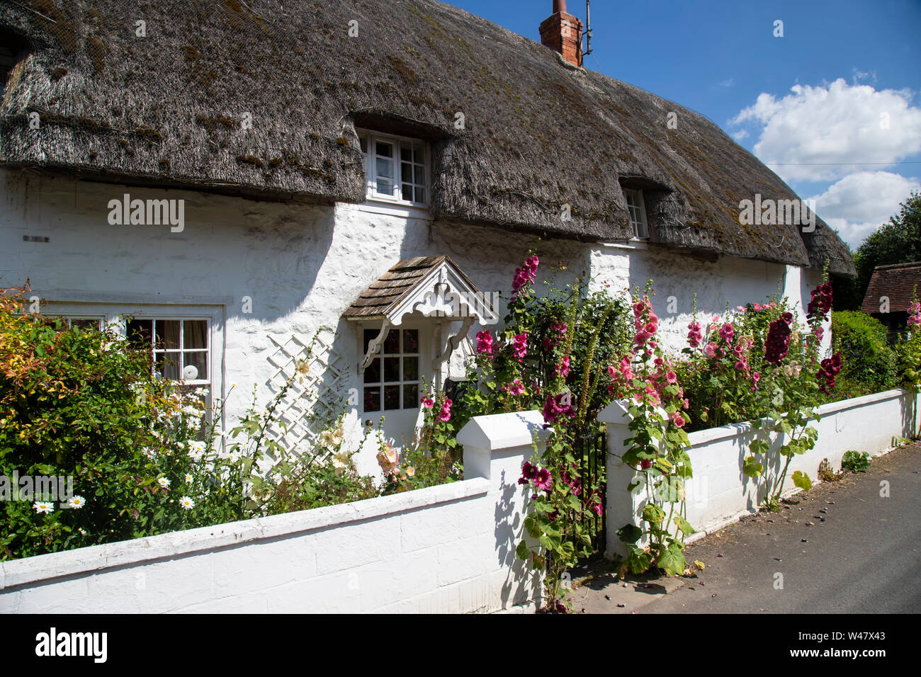Un tipico e dipinte di bianco con tetto di paglia di paese inglese cottage rifornito con inglese tradizionale con fiori in Avebury, Wiltshire. Foto Stock