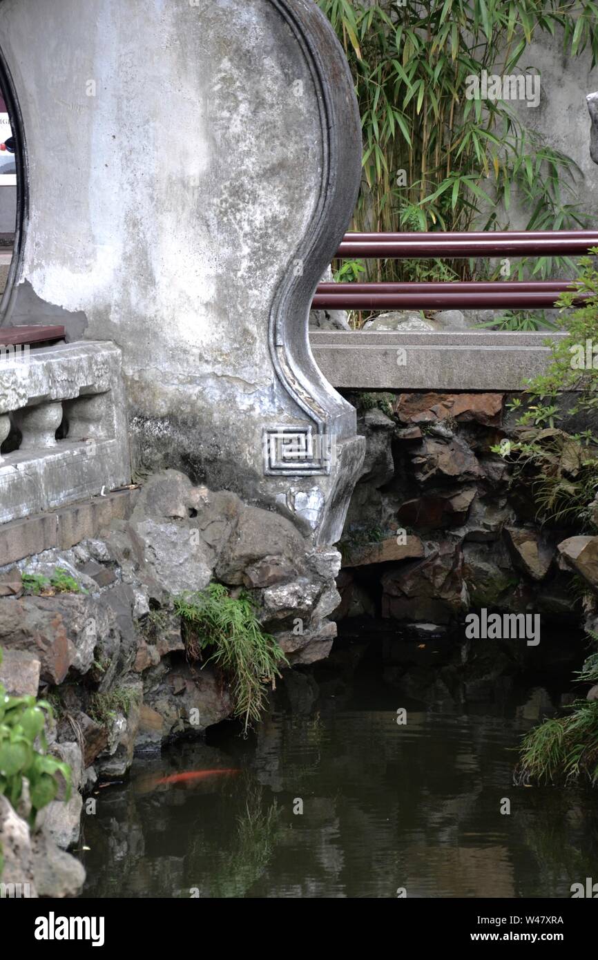Asian Garden in Cina a Shanghai. Il Footbridge con ringhiera e ornato di cemento grigio o balaustra in pietra e ringhiera sopra una tranquilla, ancora con flusso di Foto Stock