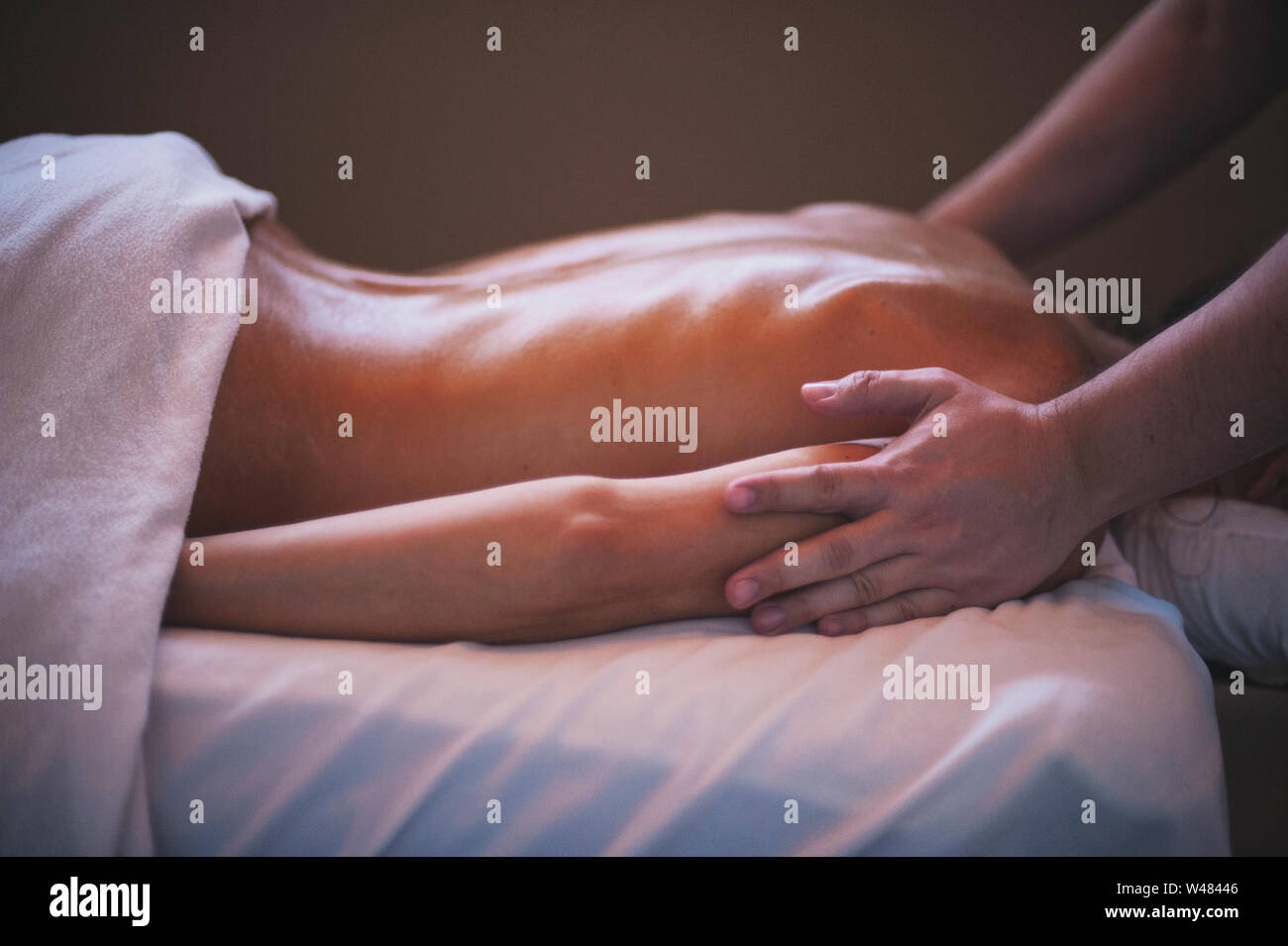 Terapista del sesso maschile dando donna client di terapia di massaggio la carrozzeria. La sua pelle è lubrificata e lei è molto adatta. La camera è moody e calmante. Foto Stock