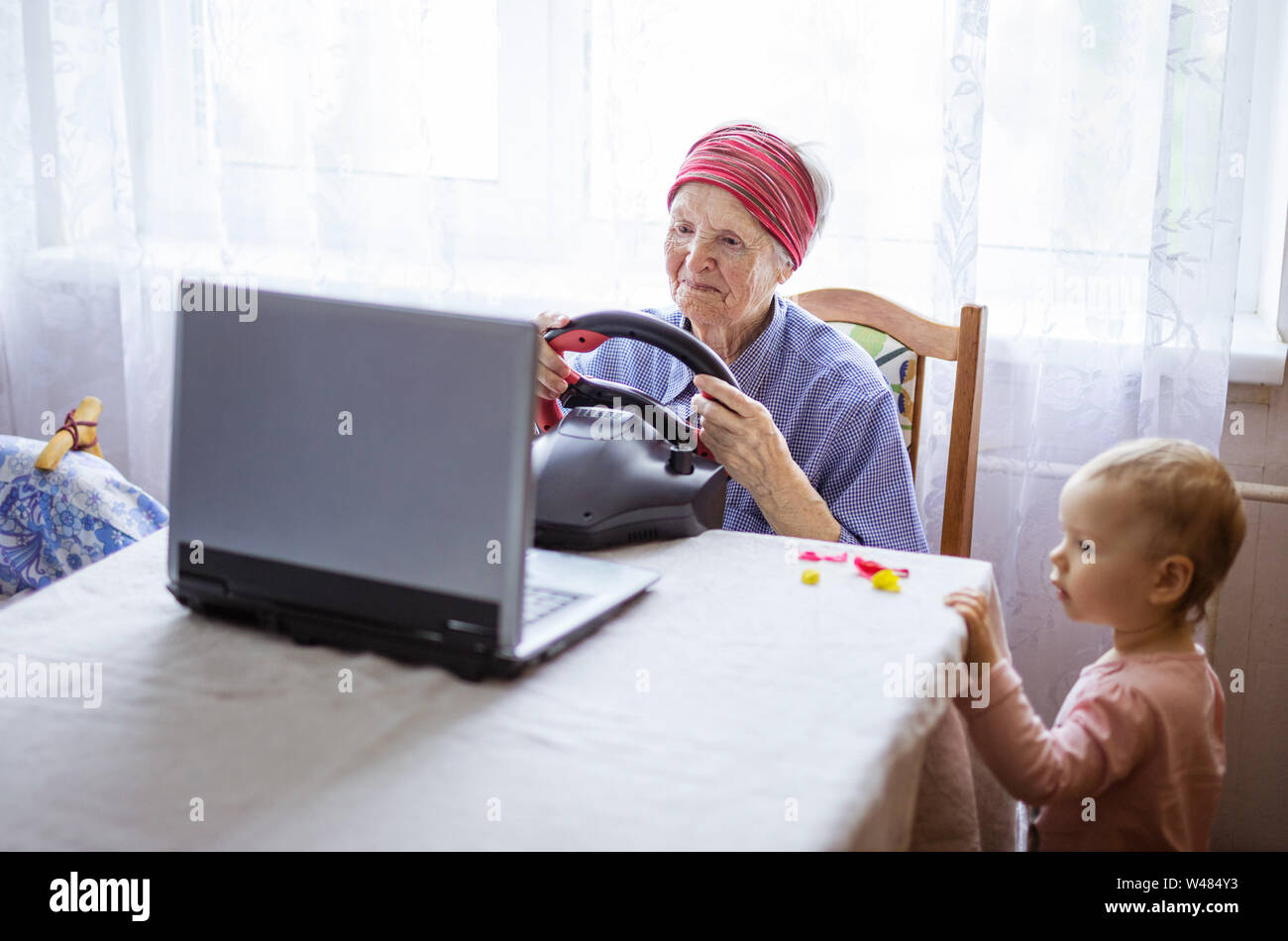 Senior donna godendo car racing video gioco sul computer portatile mentre il suo pronipote osservando il suo giocare a casa Foto Stock