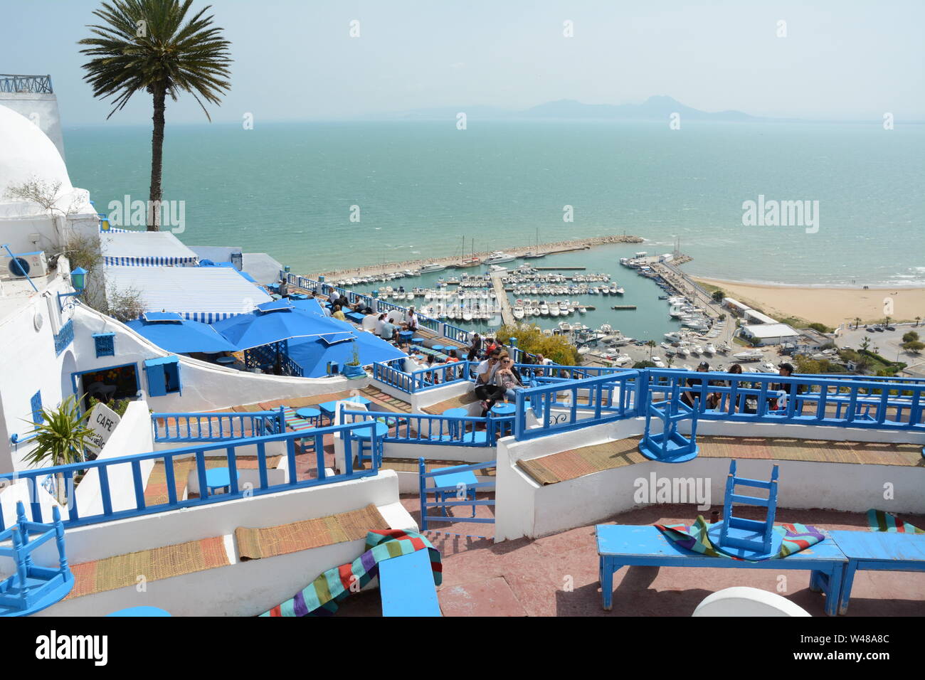 Una giovane coppia Tunsian sedersi a un tavolo del bar che si affaccia sulla acquamarina Mare Mediterraneo e il porto della città di Sidi Bou Said, Tunisi, Tunisia. Foto Stock