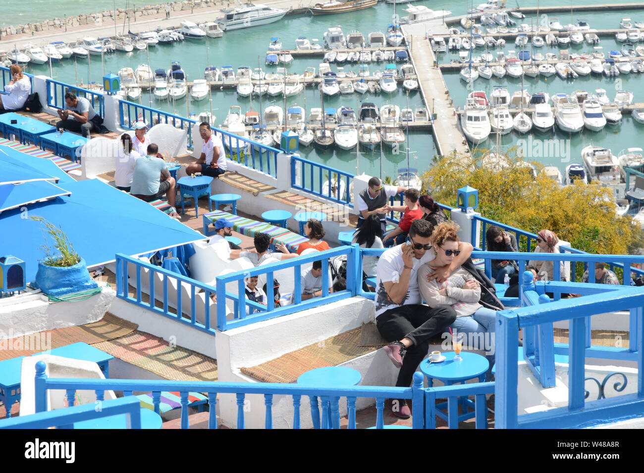 Una giovane coppia Tunsian sedersi a un tavolo del bar che si affaccia sul Mar Mediterraneo e il porto della città di Sidi Bou Said, Tunisi, Tunisia. Foto Stock